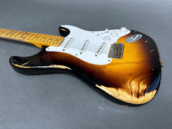 Vintage sunburst electric guitar with maple neck and white pickguard showing heavy wear and relic finish details on gray surface