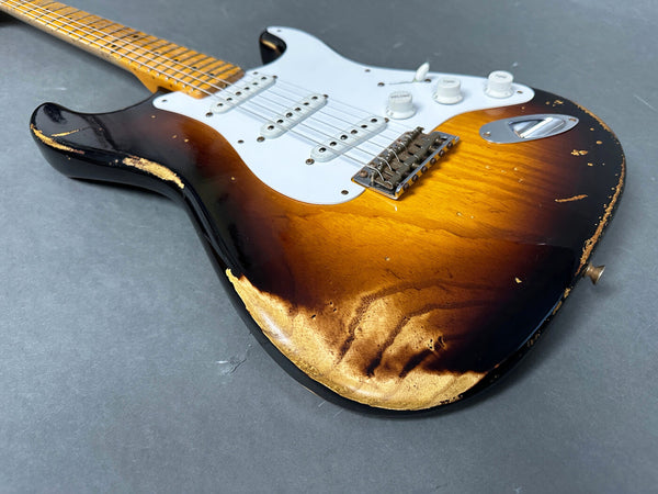 Close-up of vintage sunburst electric guitar body with worn edges and white pickguard on gray surface