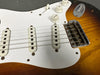 Close-up of sunburst electric guitar body showing white pickguard, single-coil pickups, control knobs for volume and tone, and bridge assembly
