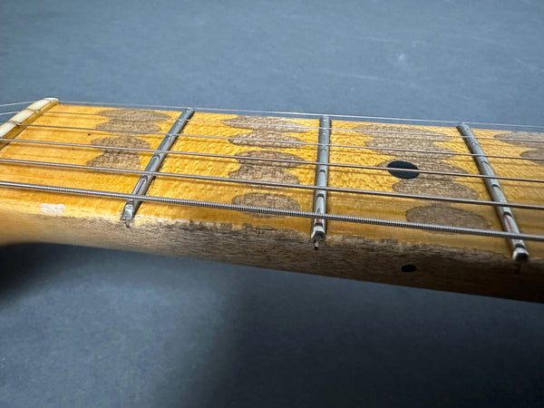 Close-up of worn vintage guitar maple neck and fretboard with metal frets and steel strings on gray background