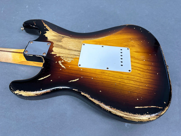 Close-up of the back body of a worn sunburst electric guitar showing heavy paint wear and a white rear cavity plate on a gray background