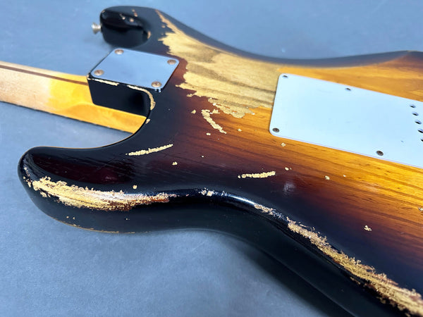 Close-up of worn sunburst electric guitar body with chipped finish and metal neck plate on gray background