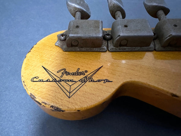Close-up of vintage Fender Custom Shop guitar headstock with worn tuning pegs and visible wood grain on natural finish