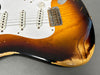 Close-up of worn sunburst electric guitar body with white pickguard and three single-coil pickups showing vintage relic finish and aging details.