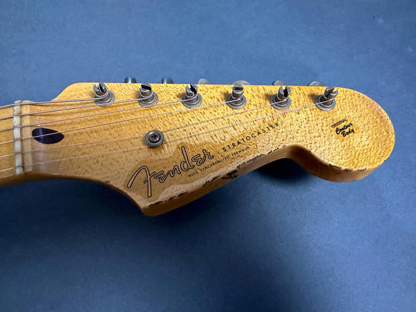 Close-up of vintage Fender Stratocaster guitar headstock with tuning pegs and worn maple neck on blue background
