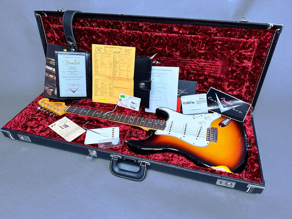 Fender Stratocaster electric guitar in sunburst finish with white pickguard inside black hardshell case lined with red plush, surrounded by Fender certificate of authenticity, warranty card, paperwork, and accessories for sale at Coffee House Guitars.
