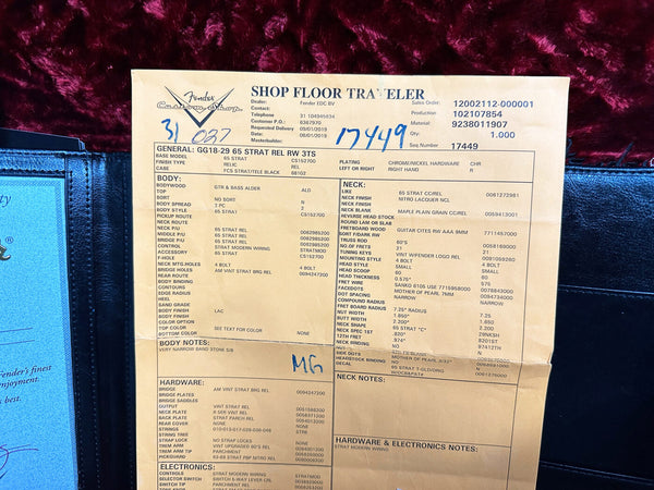 Fender Custom Shop Shop Floor Traveler specification sheet for 65 Strat Relic RW 3TS guitar with detailed body, neck, hardware, and electronics information on beige paper against dark red fabric background
