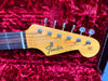 Close-up of Fender Stratocaster guitar headstock with six tuning pegs on red plush guitar case lining