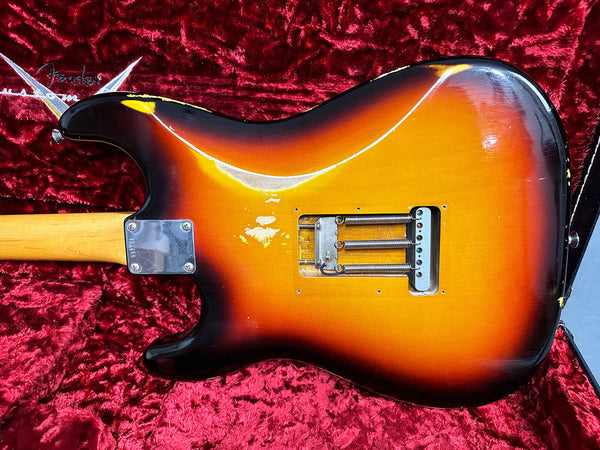 Back view of vintage sunburst Fender Stratocaster electric guitar with worn finish, showing tremolo springs, in red plush-lined Fender guitar case