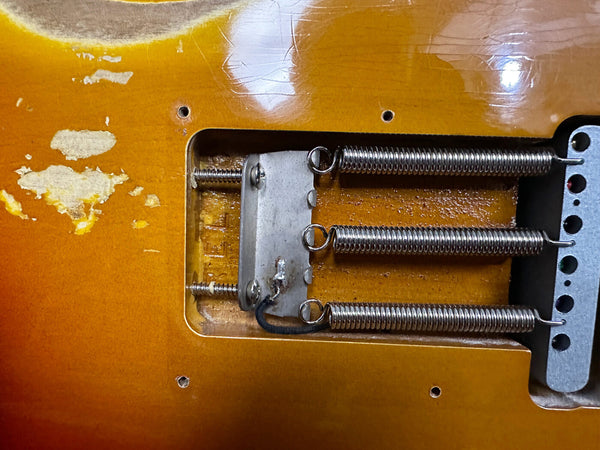 Close-up view of vintage electric guitar tremolo cavity showing three tension springs and metal claw on a sunburst finish guitar body with wear and paint chips