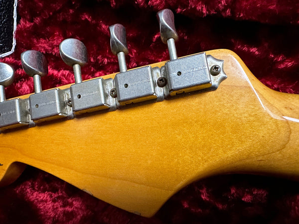 Close-up of vintage guitar headstock tuning machines showing aged metal tuners on maple wood neck against red plush background