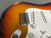 Close-up of sunburst electric guitar body showing bridge, white pickguard, volume and tone knobs, and pickups on grey background