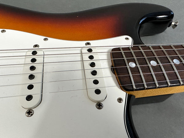 Close-up of sunburst electric guitar body showing white pickguard, two single-coil pickups, strings, and rosewood fretboard with dot inlays.
