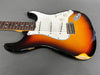 Vintage sunburst electric guitar body with white pickguard and three single-coil pickups showing worn and chipped finish on gray background