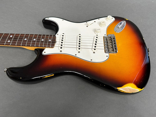 Vintage sunburst electric guitar body with white pickguard and three single-coil pickups showing worn and chipped finish on gray background