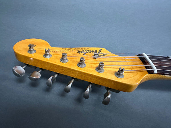 Close-up of vintage Fender Stratocaster electric guitar headstock with tuning pegs and strings on gray background