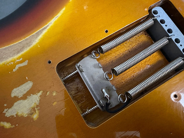 Close-up of vintage guitar tremolo cavity showing three metal springs and worn sunburst finish with paint wear and aging marks