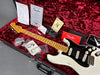Fender vintage white Stratocaster guitar with maple neck and black pickguard in red velvet-lined hardshell case with certificate of authenticity, Fender inspection checklist, tremolo arm, guitar strap, extra pickguard, and Fender manuals and tags
