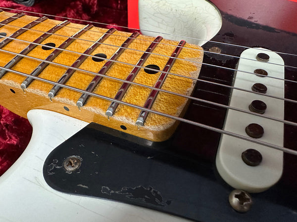 Close-up of vintage electric guitar maple fretboard with metal frets and steel strings, cream single-coil pickup, and worn black pickguard on white guitar body