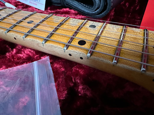 Close-up of vintage guitar neck with worn maple fretboard, metal frets, and dot inlays on red plush guitar case lining