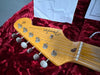 Close-up of Fender Stratocaster guitar headstock with tuning pegs and strings on red velvet case interior