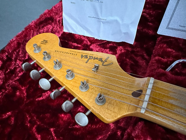 Close-up of Fender Stratocaster guitar headstock with tuning pegs and strings on red velvet case interior