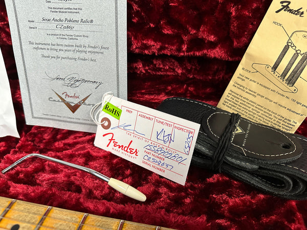 Fender Strat Ancho Poblano Relic guitar certificate of authenticity, Fender Custom Shop tag with serial number CZ528637, vintage tremolo arm, black guitar strap, and Fender tremolo adjustment instructions on red plush guitar case lining.