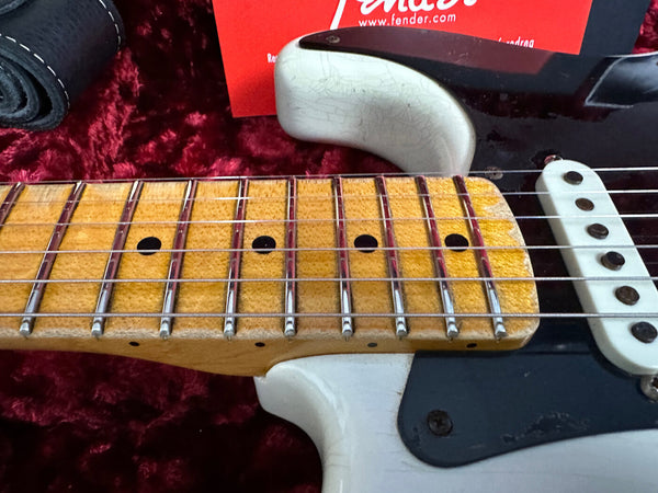 Close-up of vintage Fender Stratocaster maple fretboard showing wear and strings, resting on red plush case interior with Fender tag and black guitar strap nearby