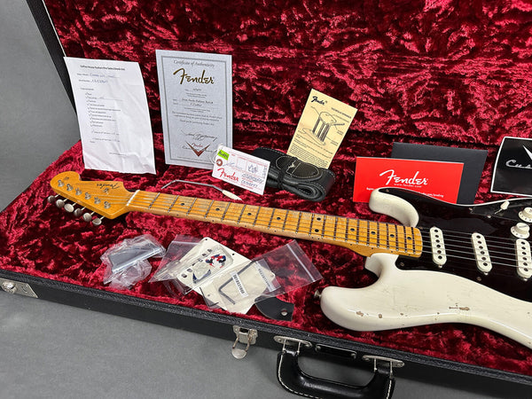 Fender electric guitar with worn white body and maple neck inside red plush-lined black hard case, accompanied by Fender certificate of authenticity, user manual, tremolo springs instruction sheet, leather strap, and various replacement parts in plastic bags.