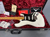 Fender Custom Shop vintage white Stratocaster electric guitar with maple neck and black pickguard in black hardshell case with red plush interior, including Fender warranty card, tremolo springs guide, black guitar strap, and extra pickup covers.
