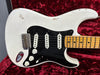 Close-up of vintage white electric guitar body with black pickguard, three single-coil pickups, and maple neck on red plush background