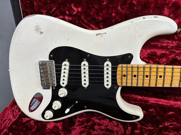 Close-up of vintage white electric guitar body with black pickguard, three single-coil pickups, and maple neck on red plush background