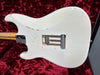 Vintage Fender electric guitar body in worn white finish showing back plate and tremolo springs on red plush background