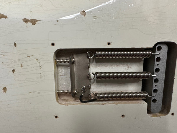 Close-up of vintage electric guitar tremolo cavity showing three tension springs and claw on aged white cracked guitar body