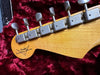 Close-up of vintage Fender Custom Shop electric guitar headstock showing tuners and logo on textured wood finish with red velvet background
