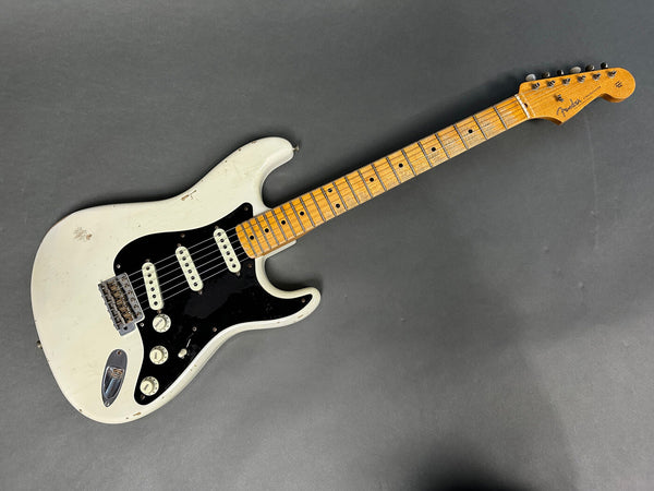 Vintage white Fender Stratocaster electric guitar with black pickguard and maple neck on gray background