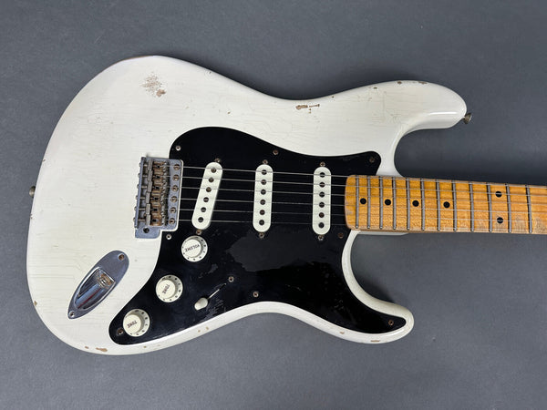 Vintage white electric guitar with black pickguard and maple neck showing wear and aged finish detail against gray background