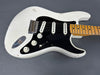 White vintage electric guitar with black pickguard, three single-coil pickups, maple neck, and volume and tone control knobs, showing wear and aged finish.