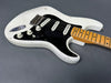 White electric guitar with black pickguard, three single-coil pickups, maple neck, and vintage-style volume and tone knobs on gray background