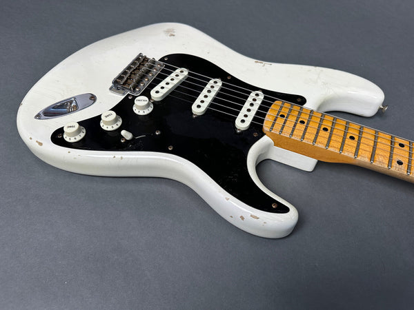 White electric guitar with black pickguard, three single-coil pickups, maple neck, and vintage-style volume and tone knobs on gray background
