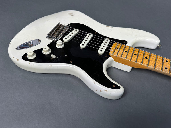 Vintage white electric guitar with black pickguard and maple neck showing wear and aging details on gray background