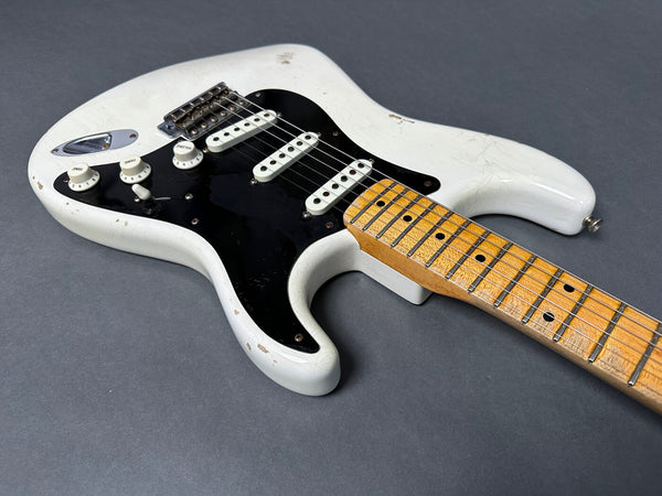 Vintage white electric guitar with black pickguard and maple fretboard showing wear and aging against gray background