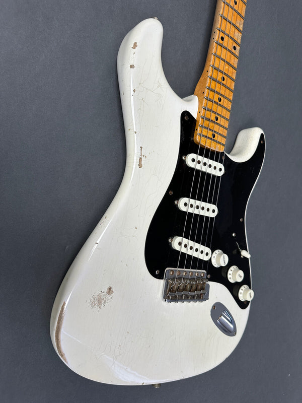 Close-up of vintage white electric guitar body with black pickguard, three single-coil pickups, maple neck, and visible wear and aging marks on the finish against gray background