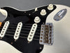 Close-up of vintage white electric guitar body showing black pickguard, three single-coil pickups, volume and tone knobs, and worn metal bridge assembly