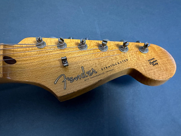 Close-up of Fender Stratocaster electric guitar headstock with tuning pegs and worn natural wood finish on blue background
