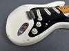 Close-up of vintage white electric guitar body showing black pickguard, three single-coil pickups, volume and tone knobs, and worn finish details