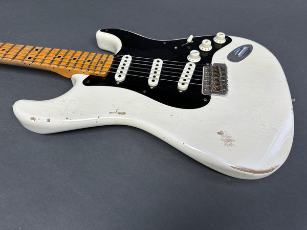 White vintage electric guitar with maple neck, black pickguard, three single-coil pickups, and worn finish showing natural wood beneath.