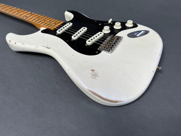 Close-up view of vintage white electric guitar with black pickguard, three single-coil pickups, maple neck and visible wear and crackling finish on body