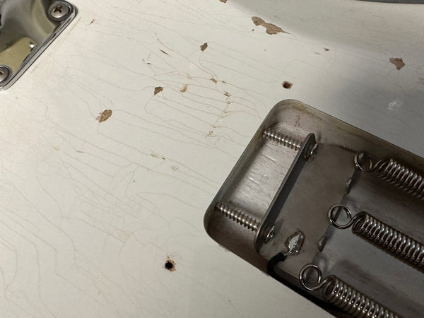 Close-up of worn, cracked white guitar body showing aging finish and metal bridge plate with springs on electric guitar