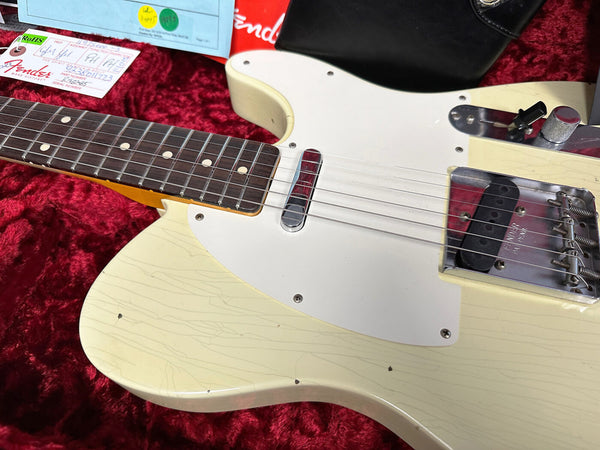 Close-up of vintage Fender Telecaster electric guitar with off-white cracked finish, rosewood fretboard, single-coil pickups, and chrome hardware on red velvet background with Fender tag and maintenance paperwork